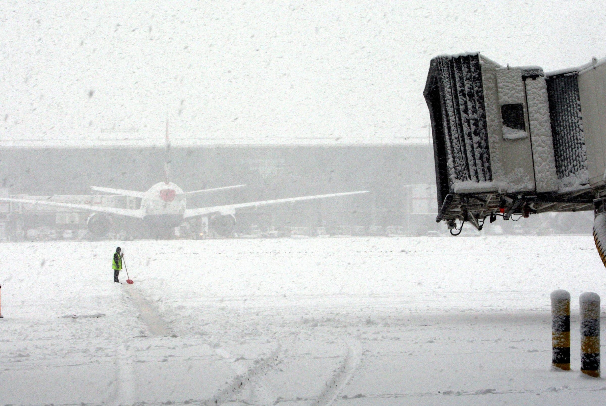 A lone worker clearing snow across a vast airport apron